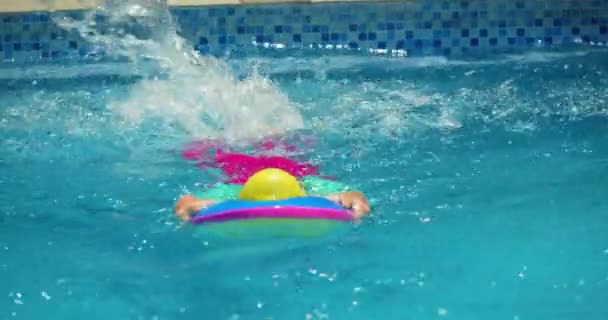 Ένα χαριτωμένο μικρό παιδί με σκουφάκια κάνει μια εργασία σε ένα μάθημα κολύμβησης στην πισίνα.. — Αρχείο Βίντεο