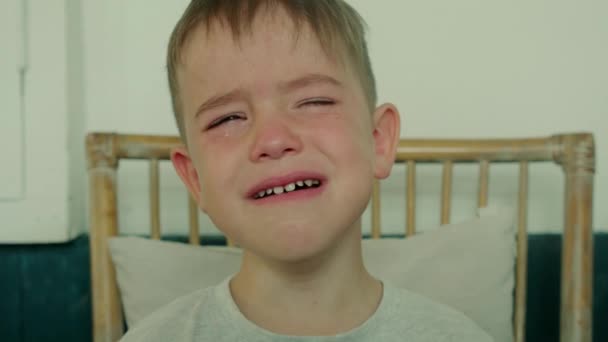 Retrato de un niño lindo con grandes lágrimas corriendo por sus mejillas, el niño se sienta a la mesa en casa y llora con la boca abierta, las lágrimas fluyen con una cara gritando. — Vídeo de stock