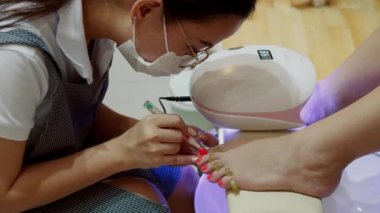 Kozmetik uzmanı prosedürü uygular, fırça darbeleri yapar, kırmızı cila uygular. Kozmitolog kuaförde bir kadına pedikür yapıyor..