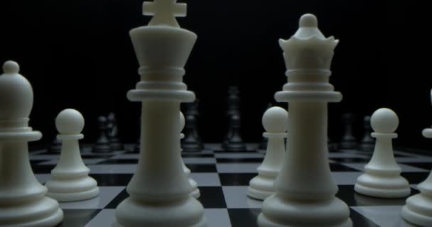 Game of chess. Filmed in a dark key. White moves with a pawn. Super-macro photography of a chessboard with chess, camera travel on a slider from white pieces to black ones. — Stock Video