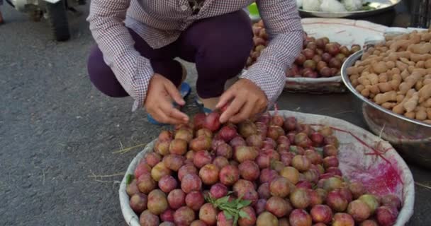 Las ancianas asiáticas venden frutas tropicales frescas, ciruelas asiáticas en el mercado callejero en la ciudad turística, sirven productos más altos y cambian las bayas hermosas a un lugar prominente para mejores ventas. — Vídeos de Stock