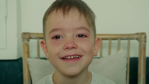 Portret van een leuke jongen met grote tranen over zijn wangen, het kind zit thuis aan tafel en lacht na het huilen. — Stockvideo