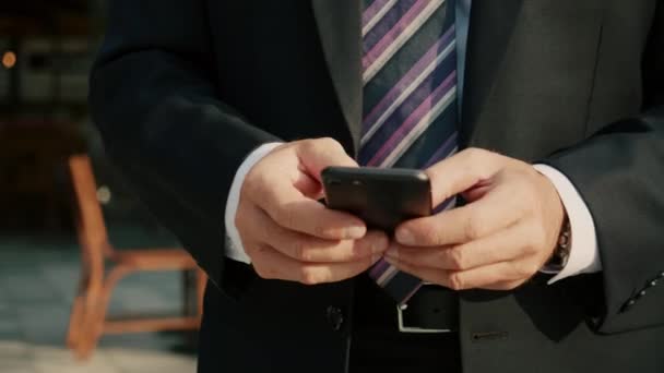 4k Erkek, telefon mesajı okuyor ya da cep telefonu için bir uygulama indiriyor. Metropolitan 'ın finans bölgesinde lüks giysiler içinde orta yaşlı iş adamı cep telefonuyla mesaj atıyor. — Stok video