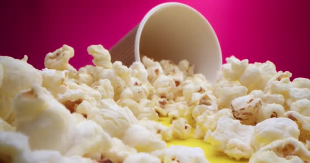 Macro obiettivo primo piano di popcorn sparsi sul tavolo, viaggiare su un cursore lungo i popcorn ad un bicchiere con popcorn su uno sfondo di lampone. Girato con telecamera ad alta velocità 4K. Rallentatore. — Video Stock