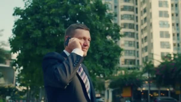 4k Un homme qui parle sur un portable dans la rue. Un homme d'affaires souriant d'âge moyen en vêtements luxueux dans le quartier financier d'une métropole utilise un téléphone portable pour négocier. — Video