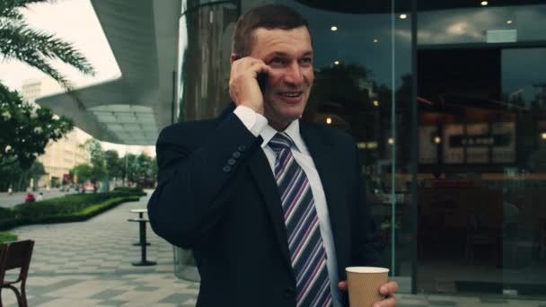 The shot moves around a businessman standing on street in the city center, who uses the phone for negotiations, ends the conversation with a smile from success after, technology, communication,success — Stockvideo