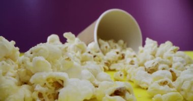 Makro mercek yakın plan patlamış mısırlar masaya saçılmış, patlamış mısır boyunca kayarak ahududu arka planında patlamış mısır olan bir bardağa gidiyor. 4K yüksek hız kamerasıyla çekildi. Yavaş çekim.