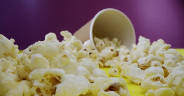 Obiektyw makro zbliżenie popcornu rozrzucone na stole, podróż na suwaku wzdłuż popcornu do szklanki z popcornem na tle malinowym. Nagrywane szybką kamerą 4K. Zwolniony ruch. — Wideo stockowe