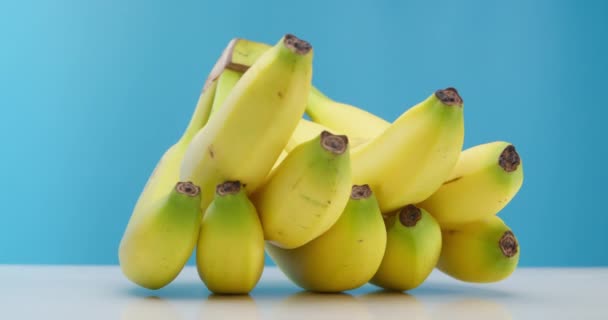 Bananas Yellow Beautiful Ripe Lying on the table on a blue background. Ripe Bananas rotate in a circle. Interesting foreshortening, stock footage. — Video Stock