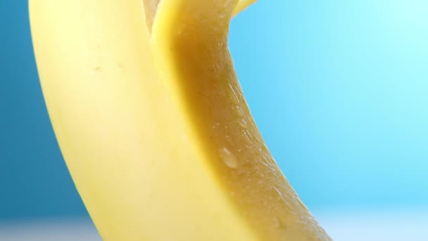 Η φρέσκια μπανάνα ξεφλουδίζει σε μπλε φόντο. Ένα θηλυκό χέρι αφαιρεί αργά ή αφαιρεί το δέρμα μιας μπανάνας, έννοια φρούτων, ξεφλουδίζοντας μια μπανάνα. — Αρχείο Βίντεο
