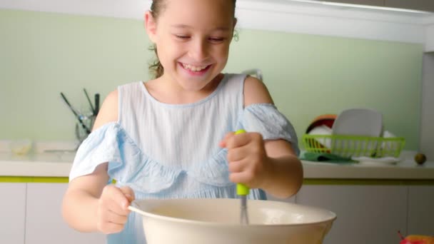 Joyeux mignon fille de huit ans cuisine dans la cuisine, quelqu'un fille est fouetter un mélange avec de la farine dans la cuisine, une petite fille fait de la pâte pour faire des crêpes ou des tartes. — Video