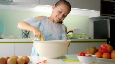 Mutfakta sekiz yaşındaki mutlu tatlı kız yemek pişiriyor, birisi mutfakta un ile karışımı kırbaçlıyor, küçük bir kız krep veya turta yapmak için hamur yapıyor..