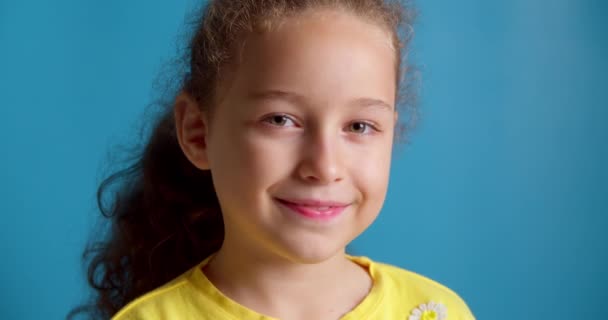 Portret Grappig meisje lachend kind kijkend naar de camera zitten op de blauwe achtergrond, schattig kind met mooi gezicht. Concept van een gelukkige jeugd. — Stockvideo