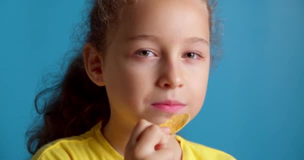 Χαριτωμένο μικρό αστείο κοριτσάκι τρώει πατατάκια, τα παιδιά παίρνουν πατατάκια και διασκεδάζουν, τα παιδιά τρώνε στην απόσταξη απολαμβάνοντας ένα νόστιμο κέρασμα στο σπίτι στην κουζίνα. — Αρχείο Βίντεο
