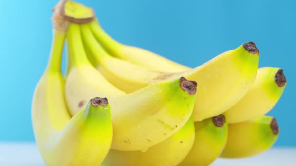 As bananas amarelas maduras bonitas com baixas da frescura encontram-se na mesa em um fundo azul. As bananas maduras giram em círculo. Ângulo interessante, imagens de estoque. — Vídeo de Stock