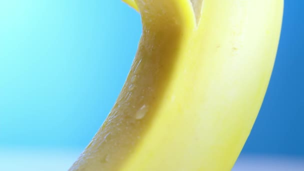 Macro lente tiro banana fresca fica descascando em um fundo azul. Uma mão feminina remove ou remove lentamente a pele de uma banana, conceito de fruta, descascando uma banana. — Vídeo de Stock