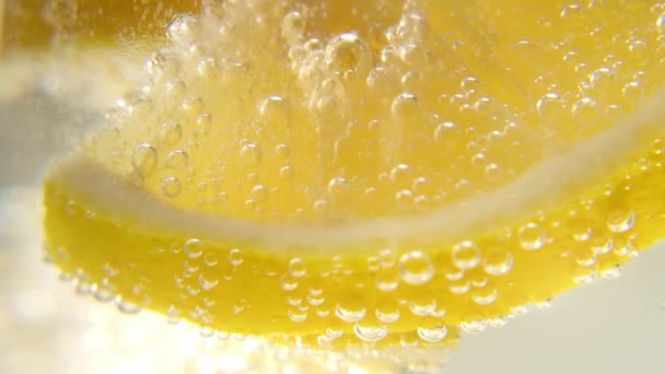 Свежий лимон добавляется в стакан игристой ледяной воды, делая освежающий прохладительный напиток. Освежающий прохладительный напиток. — стоковое видео