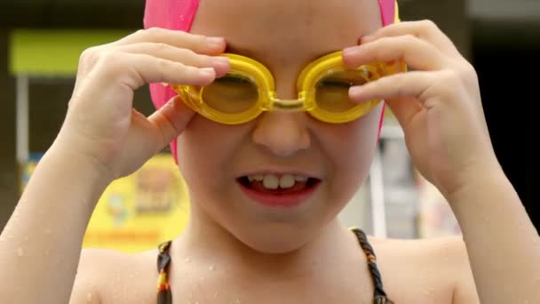 Neşeli çocuk havuzda yüzmek için yüzme gözlüğü takıyor. Yüzme gözlükleriyle havuzda mutlu küçük bir kız. — Stok video