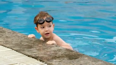 Gözlüklü neşeli çocuk havuzda banyo yapıyor. Havuzda yüzme gözlüklü şirin çocuk havuzun kenarındaki duvarı tutuyor..