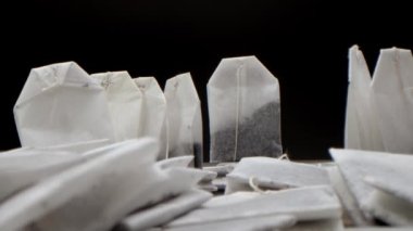 Siyah arka planda beyaz bir masanın üzerindeki süper yakın plan çay poşetleri beyaz bir çay fincanıdır. Sabah çayı yapmak. Bu çay klipsi mutfak ve mutfak projeksiyonları için uygundur.