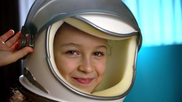 Niño juega en casa en un astronauta, retrato divertido de una niña de 8-9 años de edad en un casco de juguete espacio, niño sonriente mirando a la cámara, primer plano, piloto que viaja al espacio.Concepto de una infancia feliz — Vídeo de stock