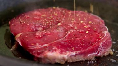 Kızartma tavasında bir parça taze mermer biftek var, çeşitli biftek baharatları serpiştirilmiş, tuz, biber, dolma biber..