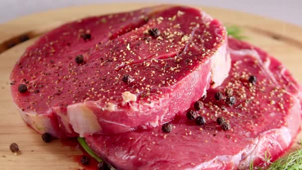 Un morceau de steak de boeuf marbré frais repose sur une planche à découper avec une variété d'herbes et d'épices pour faire le steak. — Video