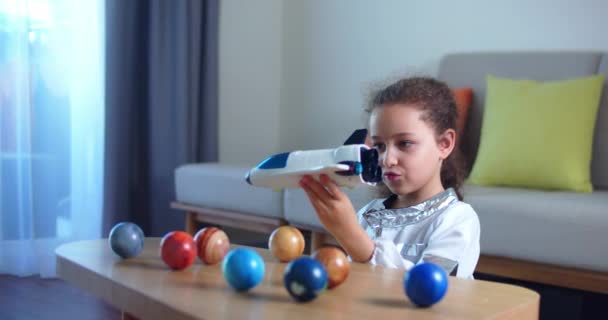 Dziecko bawi się w domu w astronaucie, zabawny portret dziewczynki 8-9 lat w zabawkowym skafandrze kosmicznym, uśmiechnięte dziecko, wystrzeliwuje rakietę kosmiczną, zbliżenie, pilota podróżującego w kosmosie. Szczęśliwego dzieciństwa — Wideo stockowe