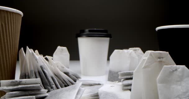 Sacchetti di tè in una tazza di tè bianco. Set di bustine di tè super close-up su un tavolo bianco su sfondo nero e una tazza di tè di carta bianca e marrone e nera. — Video Stock