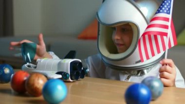 8-9 yaşlarında oyuncak bir uzay giysisi içinde, gülümseyen bir çocuğun komik bir portresi, bir uzay roketi fırlatıyor, yakın plan, uzayda seyahat eden bir pilot. Çocuk evde bir astronotla oynuyor. Mutlu çocukluk