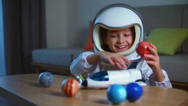 Grappig portret van een klein meisje van 8-9 jaar oud in een speelgoed ruimtepak, een lachend kind, lanceert een ruimteraket, close-up, een piloot die door de ruimte reist. Kind speelt thuis in een astronaut. Gelukkige jeugd — Stockvideo