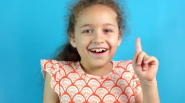 Gülümseyen mutlu küçük kız Eureka hareketi yapıyor. Düşünen genç bir çocuğun portresi. Mavi stüdyo arka planını işaret eden bir fikir..