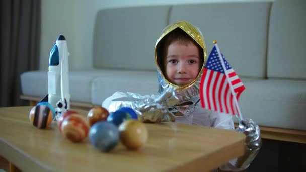 Çocuk evde bir astronotla oynuyor, 5-6 yaşlarında oyuncak uzay giysili bir çocuğun komik bir portresi, gülümseyen bir çocuk, bir uzay roketi fırlatıyor, yakın plan, uzayda seyahat eden bir pilot. Mutlu çocukluk — Stok video