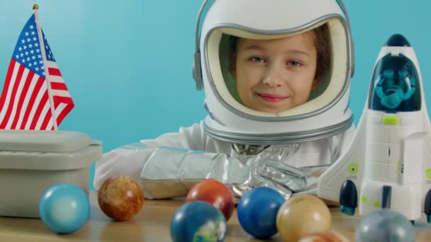 Портрет ребенка, играющего дома в астронавте, маленькая девочка 8-9 лет в костюме астронавта, улыбающийся счастливый ребенок, смотрящий в камеру, крупный план, пилот с американским флагом, путешествие в космос. — стоковое видео