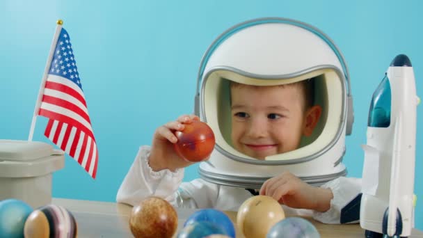 Uśmiechnięte dziecko trzymające w rękach rakietę kosmiczną Marsa, z bliska, pilota lecącego w kosmos. Dziecko bawi się w domu w astronaucie, Zabawny portret mały chłopiec 5-6 lat w zabawkowym skafandrze. — Wideo stockowe