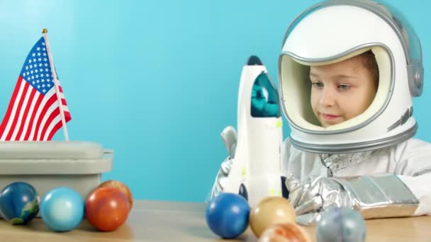 Portret dziecka bawiącego się w domu w astronaucie, dziewczynka 8-9 lat w kostiumie astronauty, uśmiechnięte szczęśliwe dziecko patrzące w obiektyw, zbliżenie, pilot z flagą amerykańską, podróż w kosmos. — Wideo stockowe