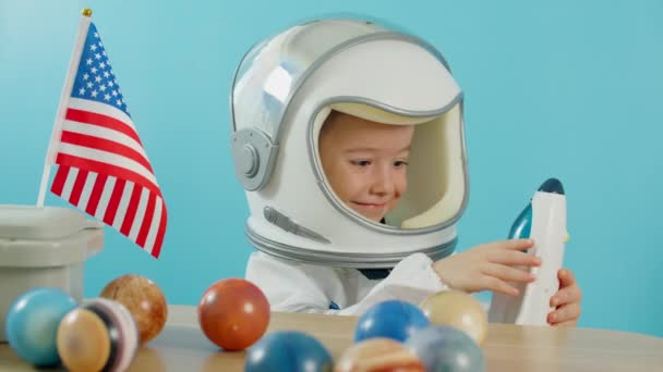 Ребенок играет дома в астронавте, портрет маленького мальчика 5 лет в костюме космонавта, улыбающийся счастливый ребенок смотрит в камеру, крупным планом, летчик с американским флагом, путешествует в космос — стоковое видео