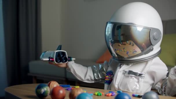 Astronotun evinde oynayan bir çocuk, astronot kostümü giymiş 5 yaşındaki bir çocuğun portresi, kameraya bakan mutlu bir çocuk, yakın plan, Amerikan bayrağı tutan bir pilot, uzaya seyahat eden — Stok video