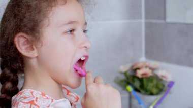 Portre mutlu, genç ve güzel bir kız sabah banyoda dişlerini fırçalıyor ve gülümsüyor. Çocuklar günlük sağlık hizmeti rutini. Beyaz dişli beyaz çocuk aynaya bakıyor. Evde izole edilmiş..