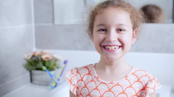 Kaukasisches Kind mit weißem Zahn, das in den Spiegel schaut und glücklich lächelt. Portrait von glücklichen netten Mädchen im Teenageralter nach dem Zähneputzen morgens im Badezimmer. Tägliche Gesundheitsversorgung für Kinder. — Stockvideo