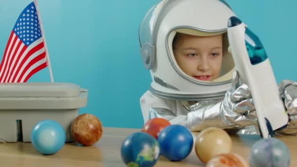 Uśmiechnięte dziecko, wystrzeliwuje rakietę kosmiczną, zbliżenie, pilot podróżujący w kosmosie. Dziecko bawi się w domu w astronaucie, zabawny portret dziewczynki 8-9 lat w zabawkowym skafandrze. Szczęśliwego dzieciństwa. — Wideo stockowe
