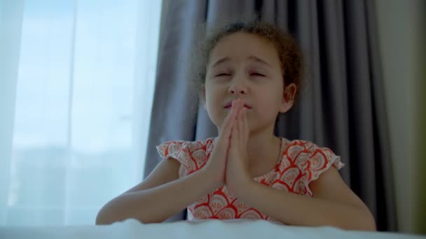 小さな女の子は彼女の部屋で祈っています。子供の概念の信仰宗教と幸せな家族の肖像画を閉じます。. — ストック動画