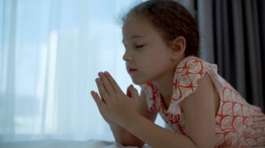 Küçük kız odasında dua ediyor.Çocuk portresi, inanç inancı ve mutlu aile kavramları. Kız çocuğu kollarını kavuşturup Tanrı 'ya dua ediyor. Katolik dua ve şükran duası ediyor..