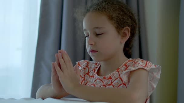 Mała dziewczynka modli się w swoim pokoju.Close up portret koncepcji dziecka religia wiary i szczęśliwej rodziny.Dziecko córka skrzyżowała ramiona, modląc się do Boga.. — Wideo stockowe