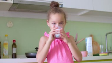 Evdeki mutfakta bir bardak süt içen tatlı küçük kız. Yavaş çekim su içen küçük kız. Yakın plan. Çocuk bardaktan süt içiyor..