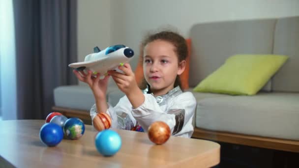 宇宙飛行士の家で遊ぶ子供、おもちゃの宇宙服の女の子8-9歳の面白い肖像画、笑顔の子供は、宇宙ロケット、クローズアップ、宇宙を旅するパイロットを起動します。幸せな子供時代 — ストック動画
