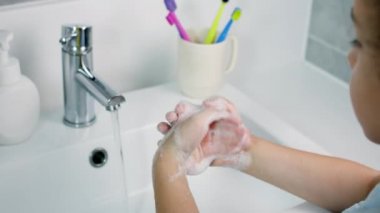 Bir çocuk ellerini sabunla yıkıyor, küçük kız elleri virüs ve bakterilerin yayılmasını önlemek için yıkıyor. Sağlık, temel ev hijyeni..