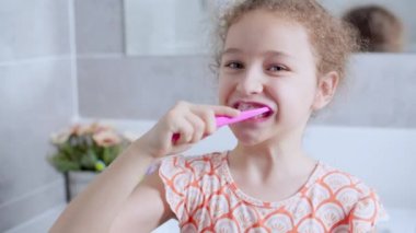 Portre mutlu, genç ve güzel bir kız sabah banyoda dişlerini fırçalıyor ve gülümsüyor. Çocuklar günlük sağlık hizmeti rutini. Beyaz dişli beyaz çocuk aynaya bakıyor. Evde izole edilmiş..