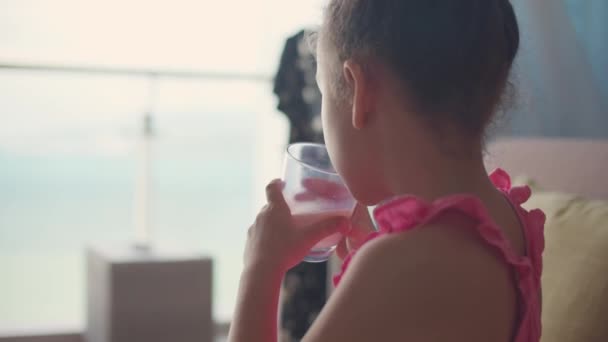 Bella bambina che beve un bicchiere di latte in cucina a casa. Ragazzina al rallentatore che beve acqua. Primo piano. Il bambino beve il latte da un bicchiere. — Video Stock