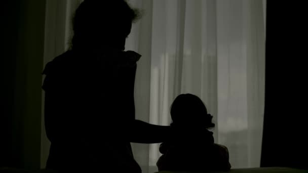 家庭用隔離室で育児。シルエット保護医療マスクの人形と女の子はベッドの上に座って、窓の外を見ています。アレルギー、 covid-19コロナウイルスのパンデミック、流行予防. — ストック動画